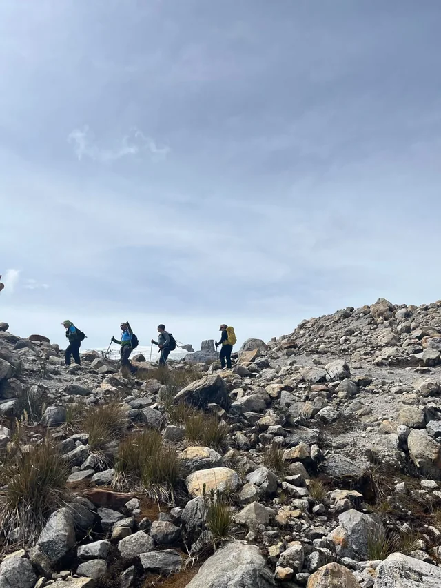 Un grupo caminando en fila sobre la morrena del Parque Nacional Natural El Cocuy, con el Púlpito del Diablo al fondo
